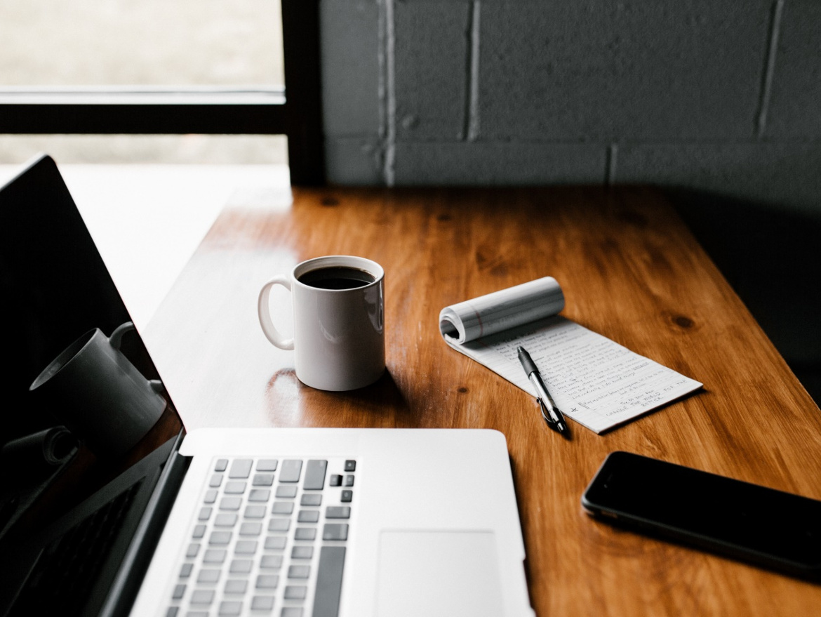 MacBoo Pro, ceramic mug, notepad and black smartphone on a table