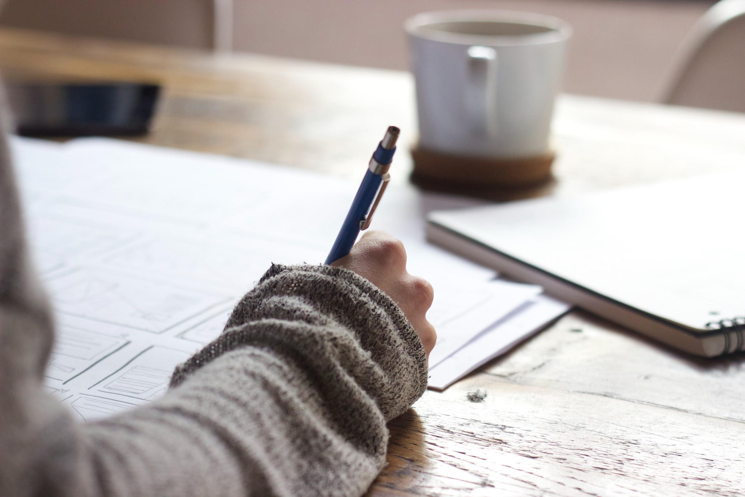 A person writing with a pen on paper 