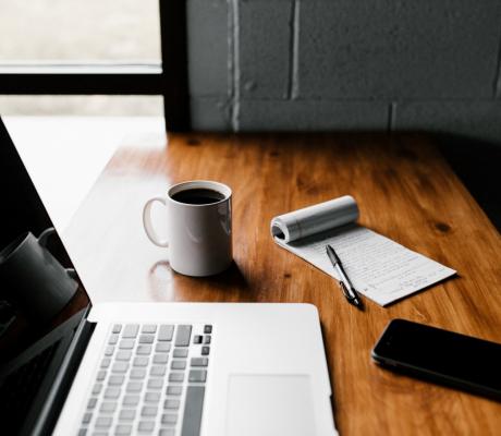 MacBoo Pro, ceramic mug, notepad and black smartphone on a table