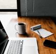MacBoo Pro, ceramic mug, notepad and black smartphone on a table